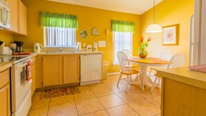 A kitchen with yellow walls, a white refrigerator, a dining table with chairs, and a hanging light fixture.