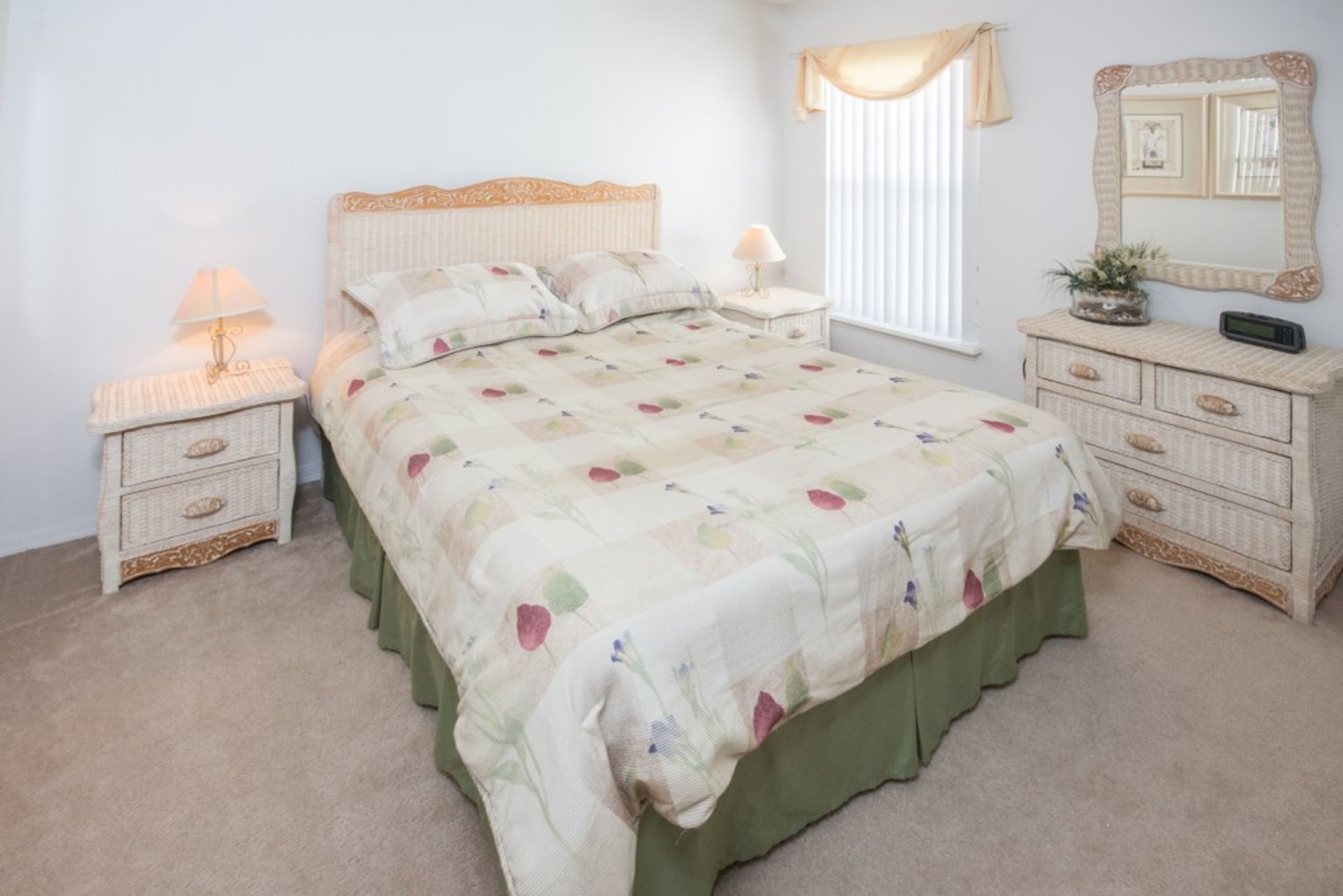 A bedroom with a bed, two bedside tables, a dresser, a mirror, and a window with curtains.