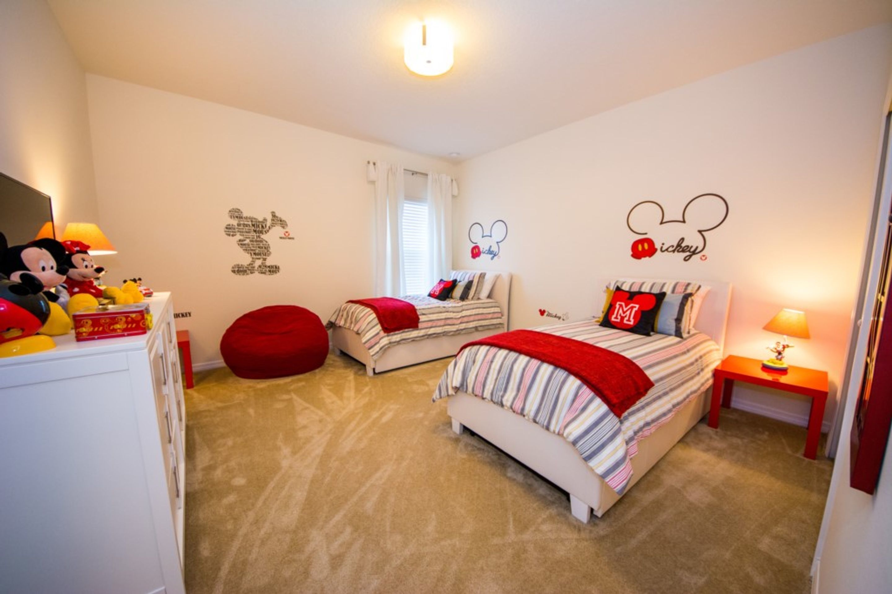 A bedroom with two beds, a red bean bag chair, Mickey Mouse wall decals, and a Mickey Mouse sign.