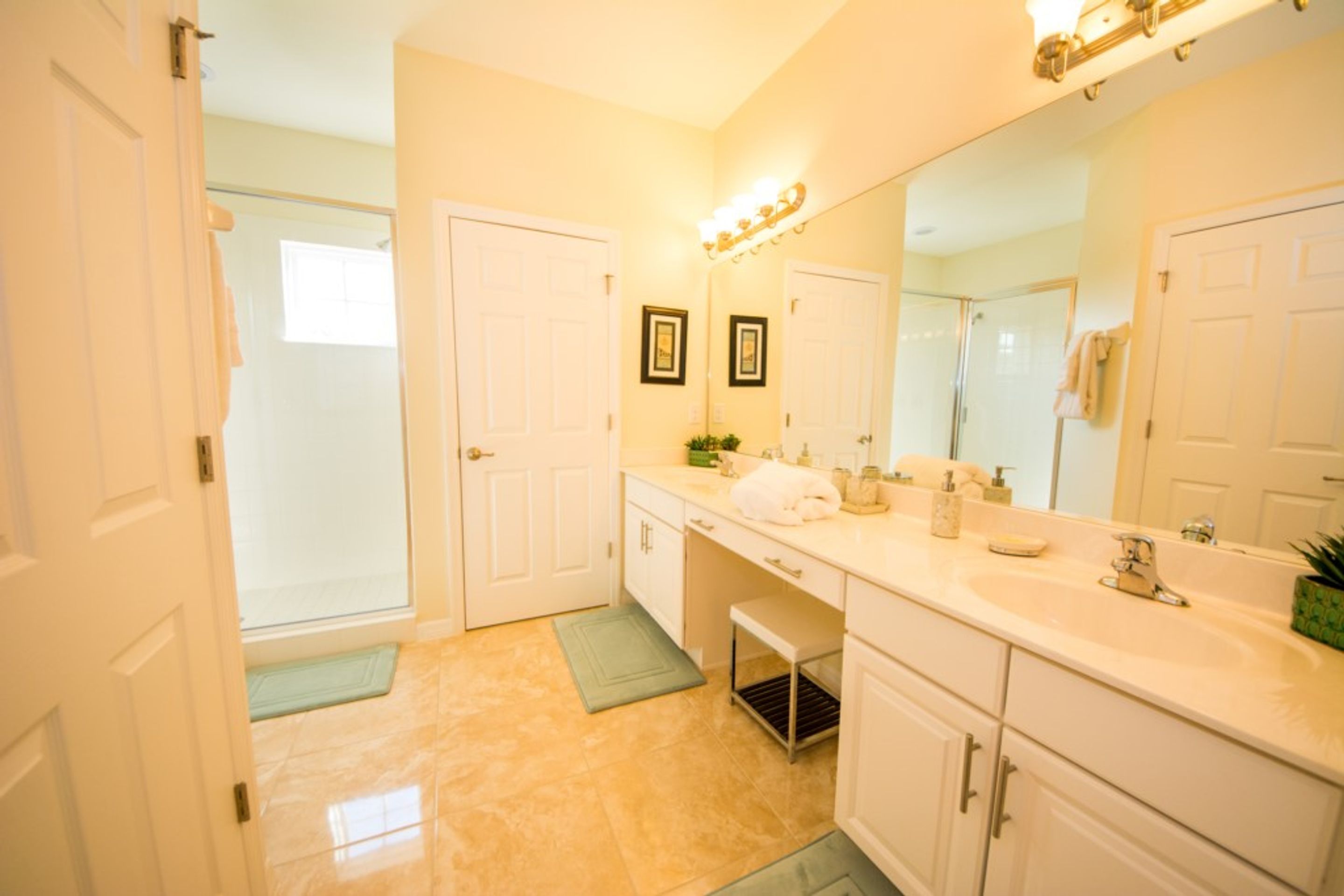 A bathroom with a large mirror, white cabinets, a sink, and a shower area.