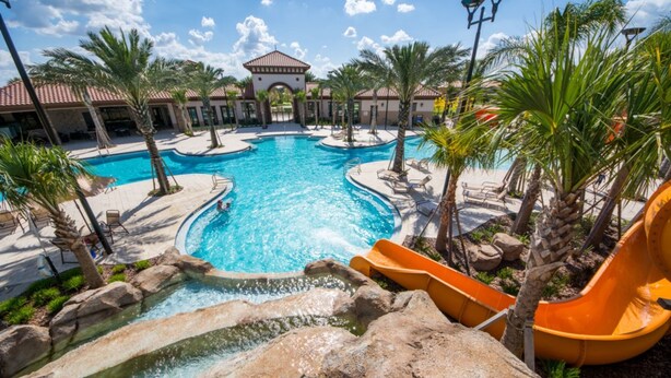 A large outdoor swimming pool with a water slide, surrounded by palm trees and lounge chairs. - Solterra 4043 (Davenport)