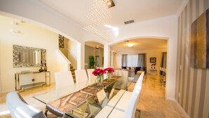A spacious dining area with a long table, white chairs, and a glass top. There is a staircase leading to another level and a large mirror on the wall. - Solterra 4043 (Davenport)