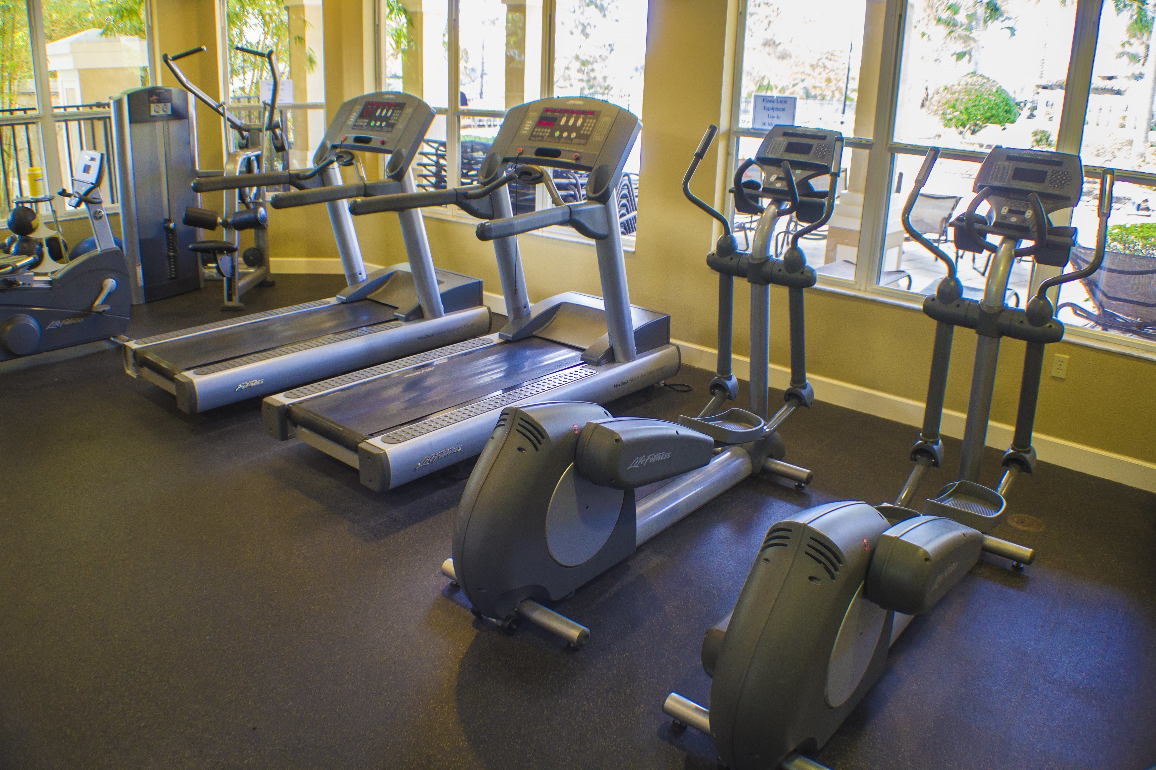 Ein Fitnessstudio mit verschiedenen Trainingsgeräten, darunter Laufbänder, Crosstrainer und Fahrräder.