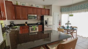 A kitchen with wooden cabinets, a stainless steel refrigerator, a microwave, and a large island with a glass top.