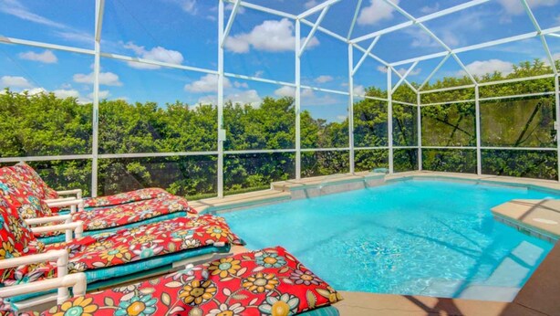 An indoor swimming pool with a glass ceiling, surrounded by lounge chairs with floral cushions. - Highlands Reserve Golf & Country Club 447 (Davenport)