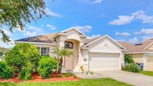 A single-story house with a garage, surrounded by a well-maintained lawn and a variety of shrubs and trees. - Highlands Reserve Golf & Country Club 447 (Davenport)