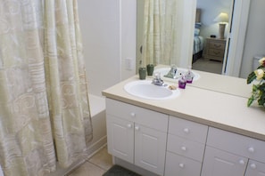 A bathroom with a white sink, mirror, and cabinet. There is a shower curtain with a leaf pattern. - Windsor Palms 2334 (Kissimmee)
