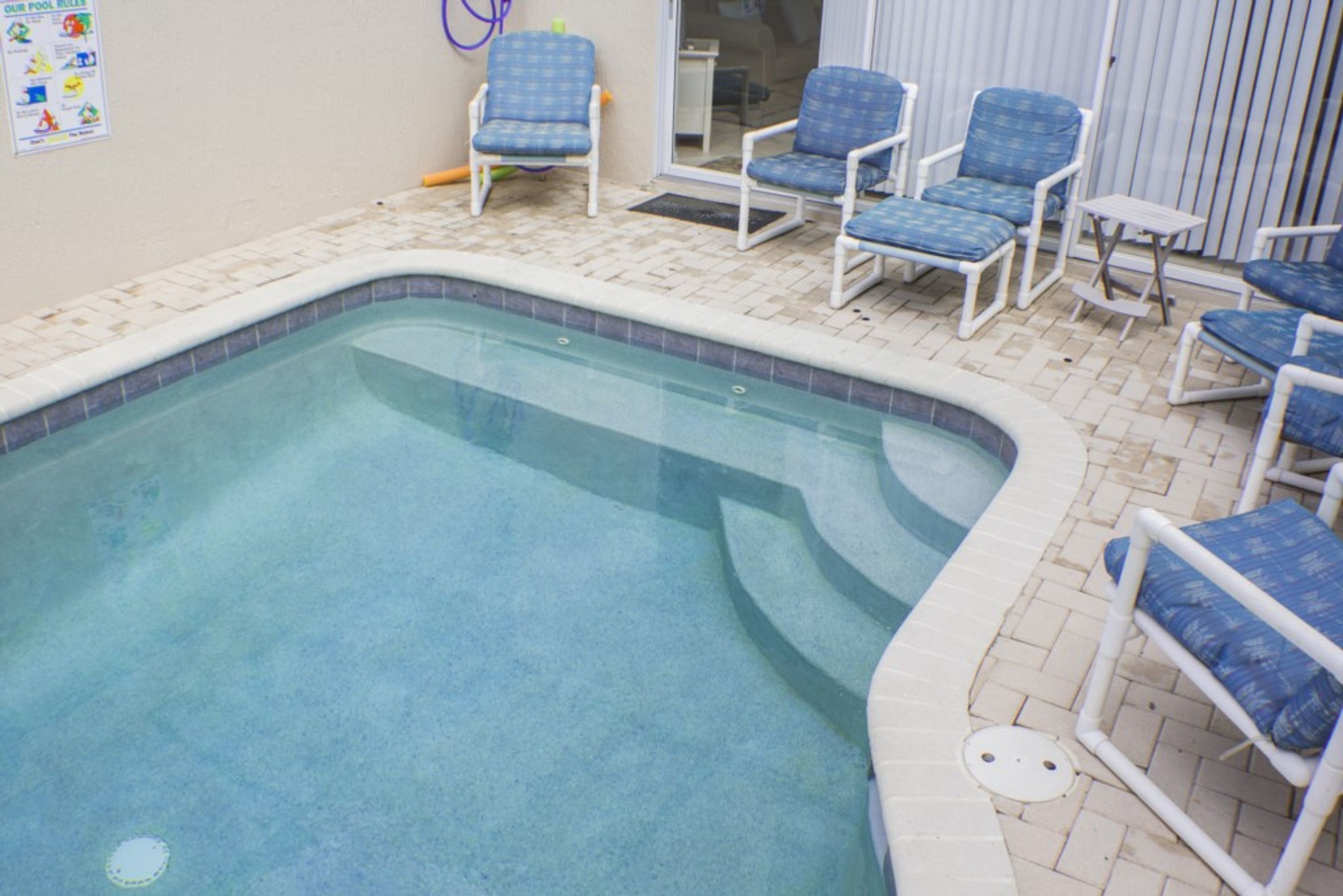 A pool area with a tiled edge, blue lounge chairs, and a poster on the wall.