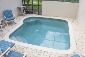 A rectangular hot tub with a tiled edge, surrounded by a brick patio. There are two lounge chairs and a small table. - Windsor Palms 2334 (Kissimmee)