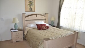 A bedroom with a wooden bed, two bedside tables with lamps, a nightstand, a framed picture on the wall, and a window with sheer curtains. - Highlands Reserve Golf & Country Club 1111 (Davenport)