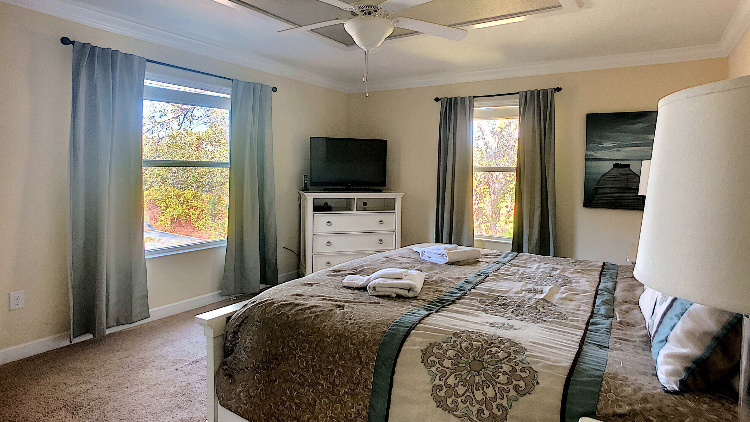A bedroom with a bed, a television on a dresser, and a window with curtains.