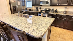 A kitchen with granite countertops, stainless steel appliances, dark cabinetry, and a built-in oven. - Paradise Palms 8955 (Kissimmee)