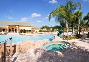 A swimming pool area with a water slide, palm trees, and a building with a tiled roof.