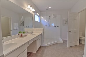 A modern bathroom with a large mirror, a walk-in shower, and a toilet visible through an open door.
