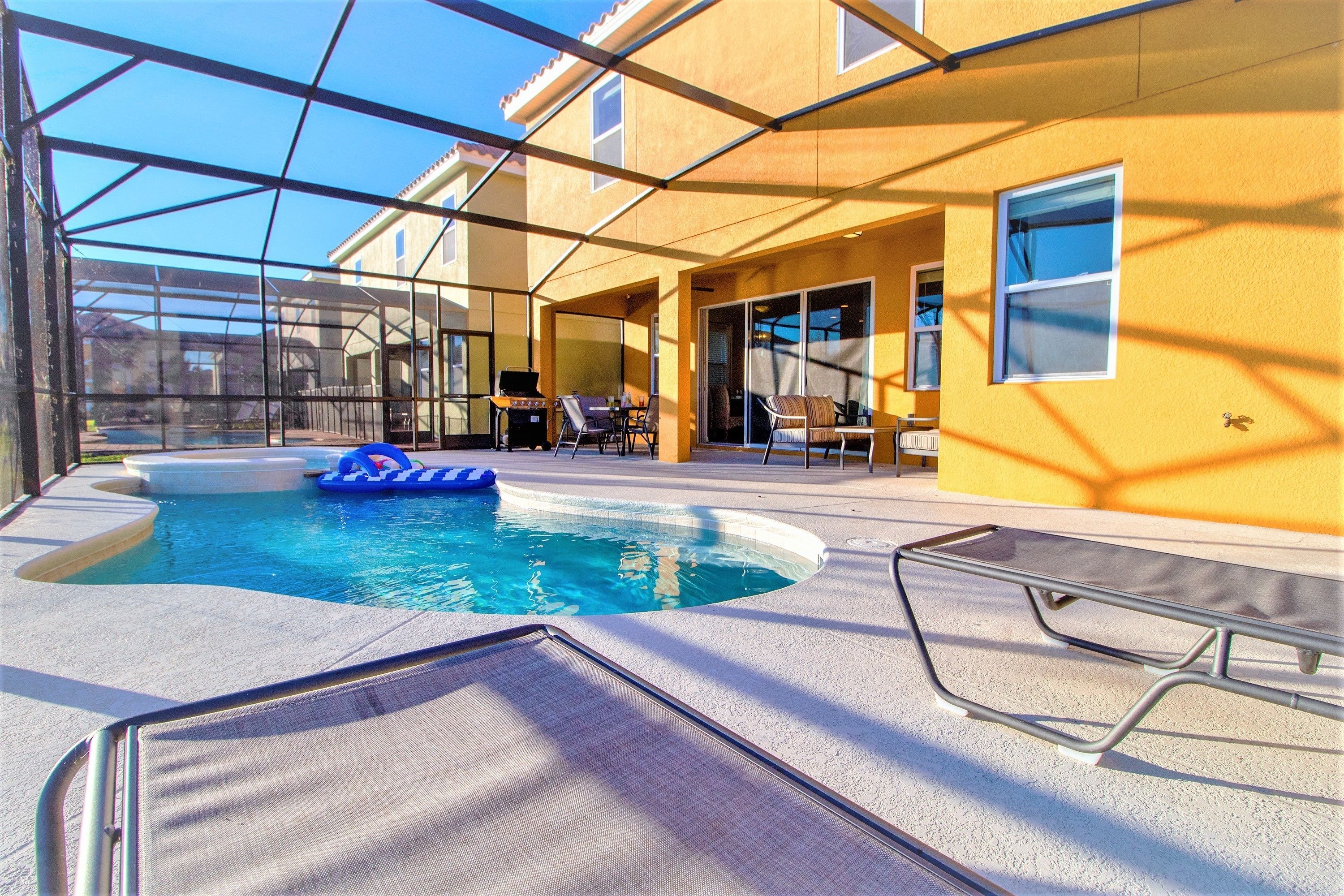 A pool area with a clear view of the pool, lounge chairs, and a barbecue grill.