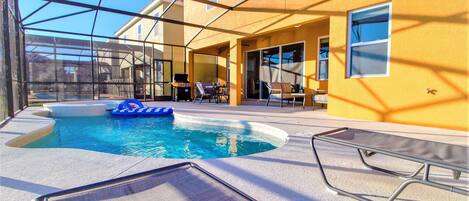 A pool area with a clear view of the pool, lounge chairs, and a barbecue grill.
