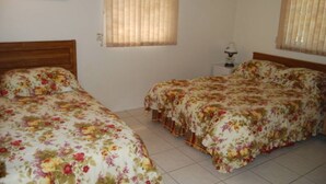 A bedroom with two single beds and a larger bed, all with floral bedding. There are two windows with blinds, a bedside table with a lamp, and a framed picture on the wall. - Bonita Springs 23 (Bonita Springs)