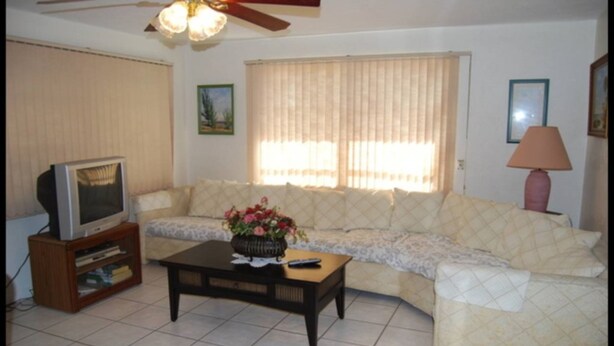 A living room with a sofa, a television on a wooden stand, a coffee table with a vase of flowers, and a lamp. - Bonita Springs 23 (Bonita Springs)