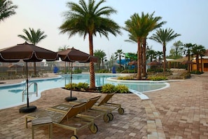 A poolside area with lounge chairs, umbrellas, and palm trees.