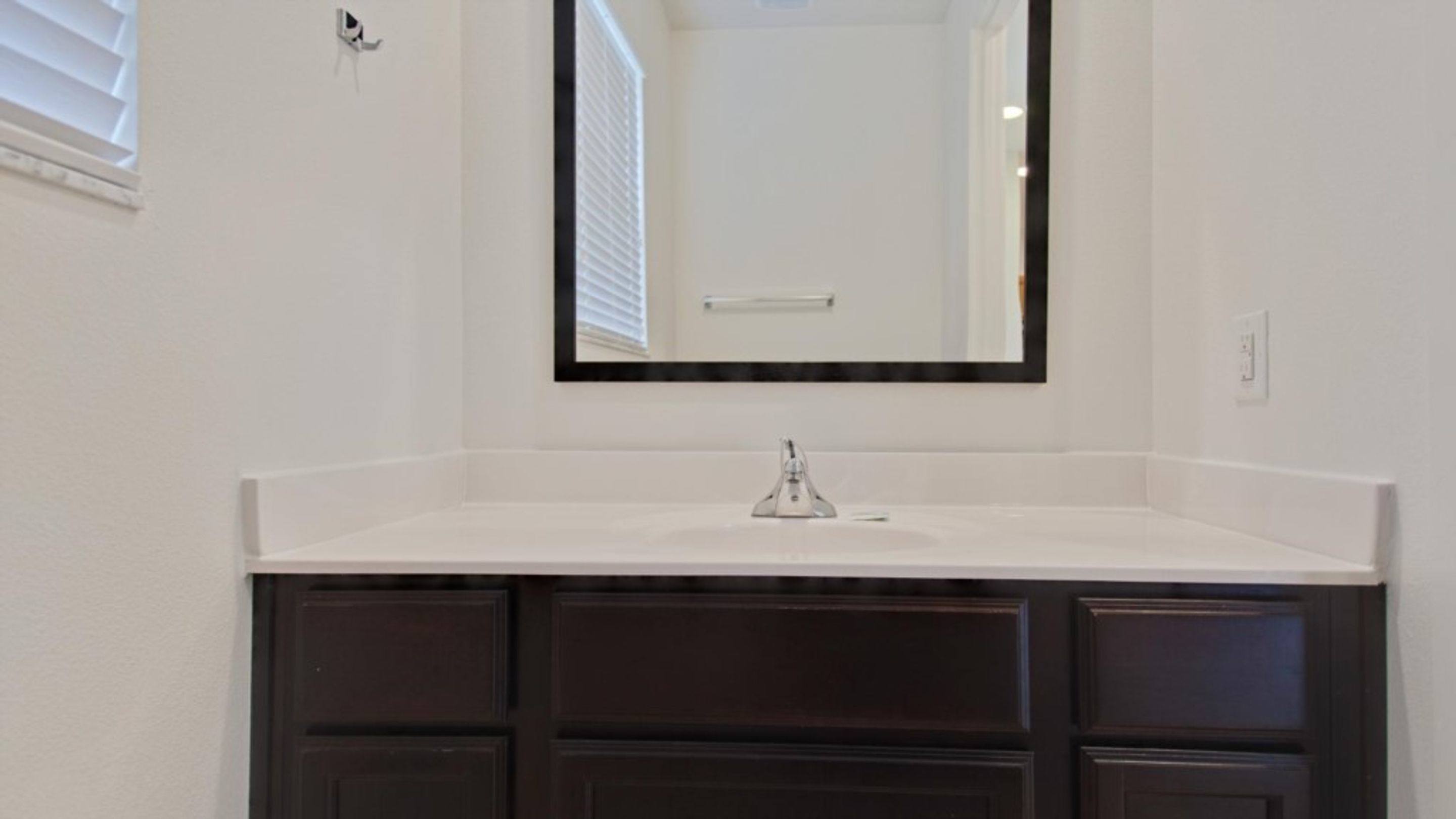 A bathroom with a white vanity, dark cabinets, and a mirror above the sink.