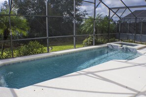 Une piscine rectangulaire dotée d’une plage blanche, entourée d’une clôture métallique, et bordée d’une végétation luxuriante.