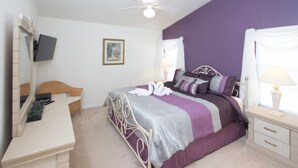 Een slaapkamer met een bed, een bureau, een stoel, een spiegel, een plafondventilator en een raam met gordijnen.