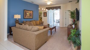 A living room with a beige sofa, a coffee table, and a lamp. There is a painting on the wall and a plant on the side.