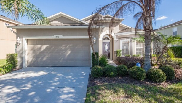 A residential house with a garage, a well-maintained lawn, and a palm tree.