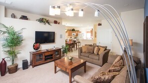 A living room with a sofa, coffee table, TV, and a dining area in the background.