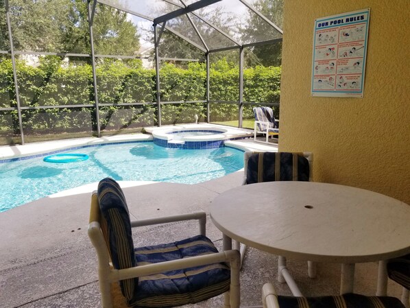 A covered pool area with a hot tub, lounge chairs, and a table.