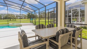 A covered outdoor patio with a pool, a table with chairs, and a view of a golf course.