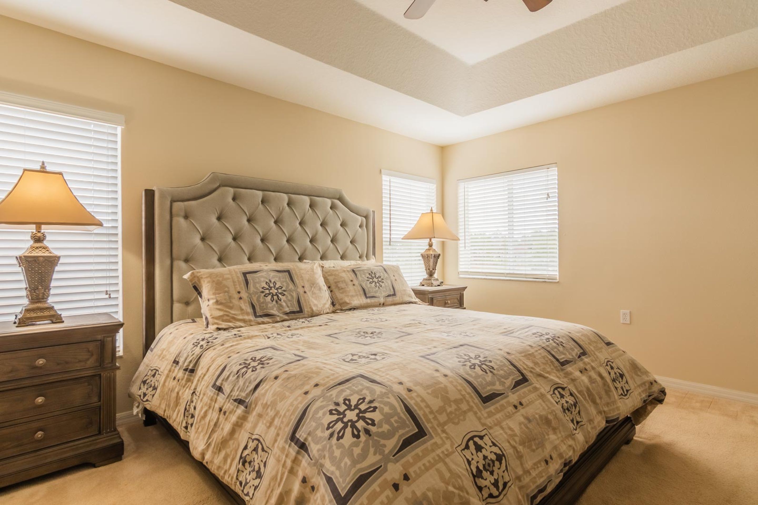 A bedroom with a tufted headboard, a patterned bedspread, two bedside lamps, and a nightstand with drawers.