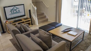 A living room with a sofa, a coffee table, and a TV displaying 'Florida Vacation Homes'. - Encantada Resort 3076 (Kissimmee)