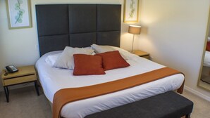 A neatly made bed with a dark headboard, a brown throw blanket, and two red pillows. There is a bedside table with a lamp and a phone. - Encantada Resort 3076 (Kissimmee)