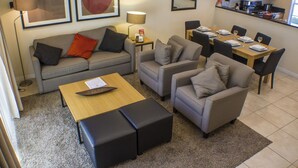 A modern living room with a grey sofa, two armchairs, a wooden coffee table, and a dining area with a table set for four. - Encantada Resort 3076 (Kissimmee)