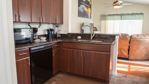 A modern kitchen with dark wood cabinets, a black dishwasher, and a granite countertop. - Wellington 132 (Davenport)