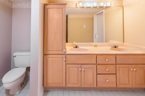 A bathroom with wooden cabinets, a double sink, and a mirror with lights.