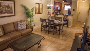 A living room with a brown sofa, a glass-top coffee table, and a dining area with a wooden table and chairs. - Bella Piazza 906 - 414 (Davenport)