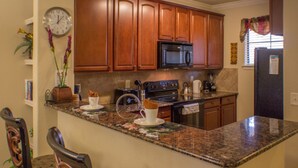 A kitchen with wooden cabinets, a microwave, a coffee maker, and a clock on the wall. - Bella Piazza 906 - 414 (Davenport)