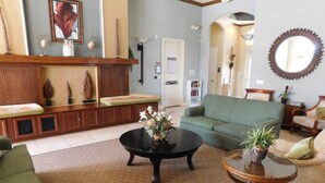 A living room with a green sofa, a leopard print armchair, a coffee table with a vase, and a wooden cabinet with decorative items. - Coral Cay 2475 (Kissimmee)