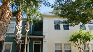 A two-story building with a green and white facade, a brick pathway, and palm trees. - Coral Cay 2475 (Kissimmee)
