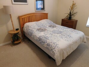 A bedroom with a wooden bed frame, a floral bedspread, a bedside table with a lamp, and a small plant. - Coral Cay 2475 (Kissimmee)