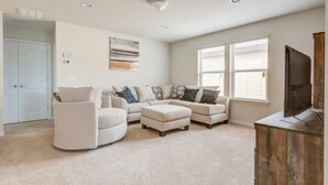 A living room with a sectional sofa, ottomans, a flat-screen TV, and a wooden cabinet. - Windsor at Westside 1828 (Kissimmee)