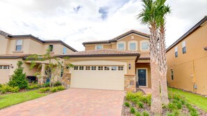 A residential building with a garage, a driveway, and a well-maintained garden with palm trees and shrubs. - Windsor at Westside 1828 (Kissimmee)