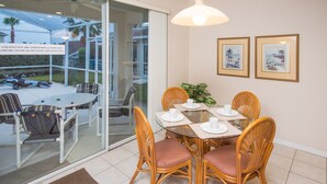 A dining area with a glass door leading outside, wicker chairs, a round table, and two framed pictures on the wall. - Highlands Reserve Golf & Country Club 349 (Davenport)
