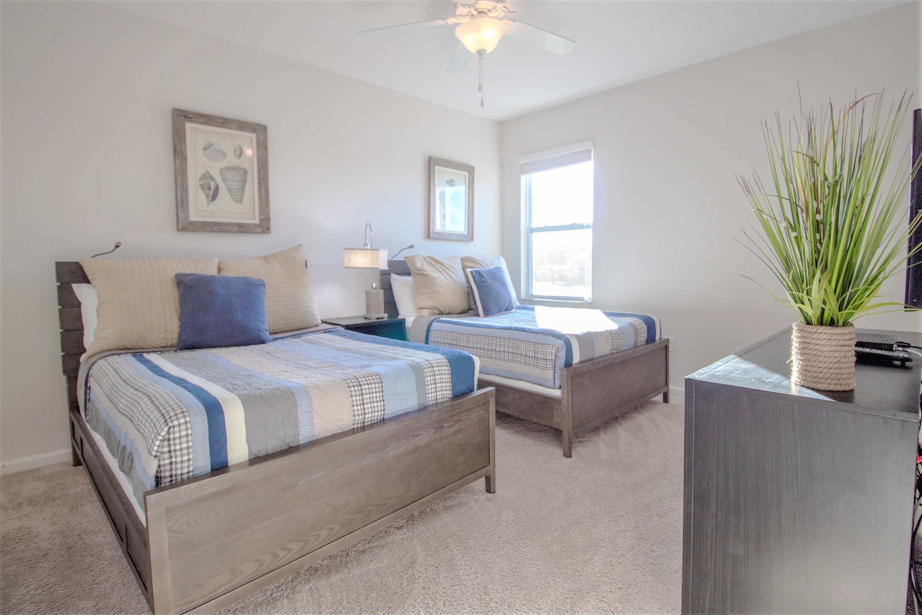 A bedroom with two beds, a desk, and a ceiling fan.