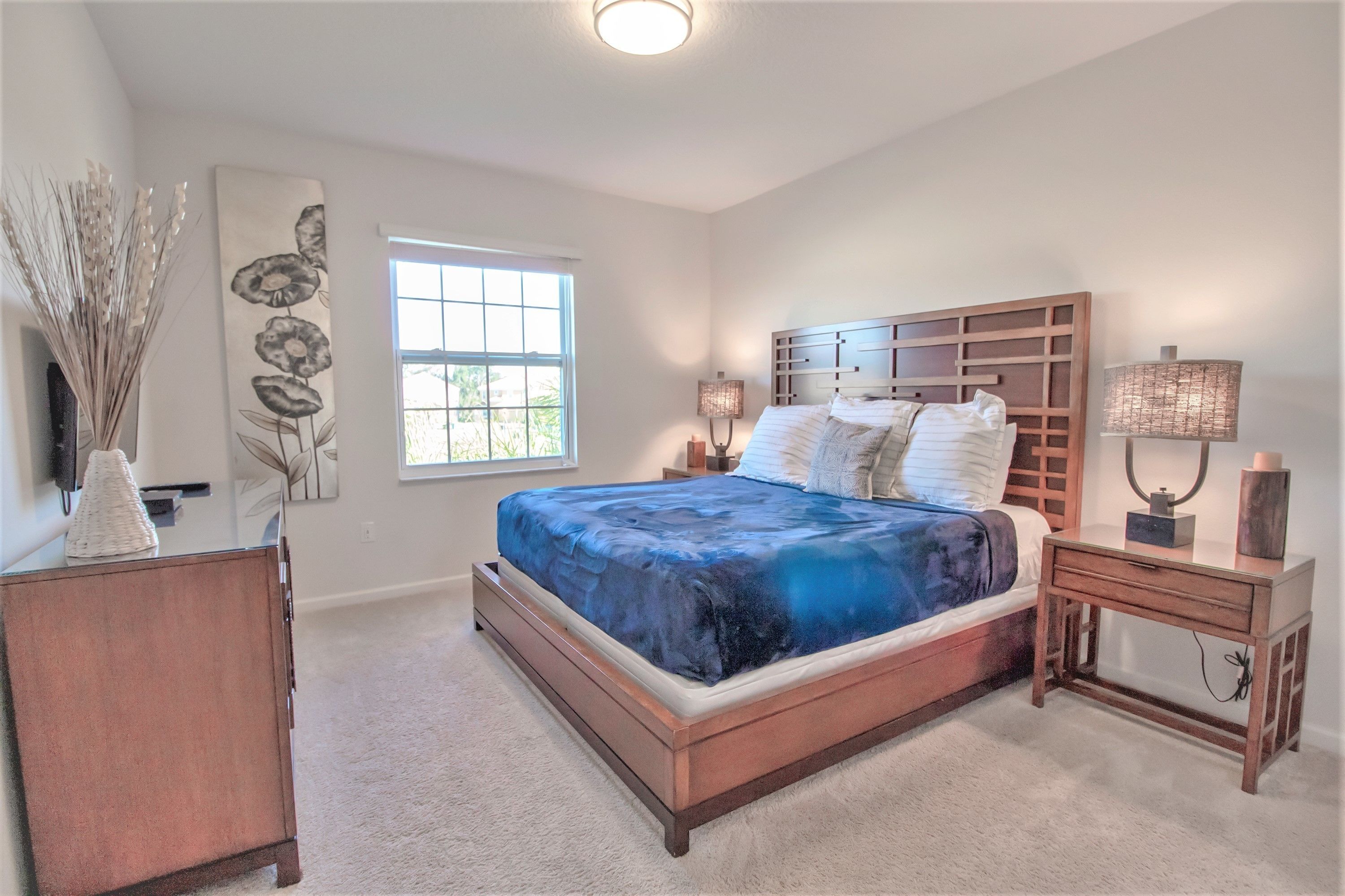 A bedroom with a bed, bedside tables, a nightstand, a wall-mounted lamp, and a window.