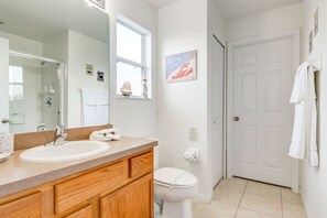 A bathroom with a wooden vanity, white sink, and toilet. There is a window with a ship decoration and a framed picture on the wall. - Southern Dunes 2901 (Haines City)