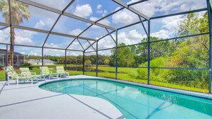 A swimming pool with a glass enclosure, surrounded by green lawn and trees. - Clear Creek 909 (Clermont)