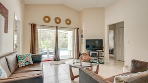 A living room with a sofa, a glass coffee table, a television, and a view of the outdoors through a sliding door. - Clear Creek 909 (Clermont)